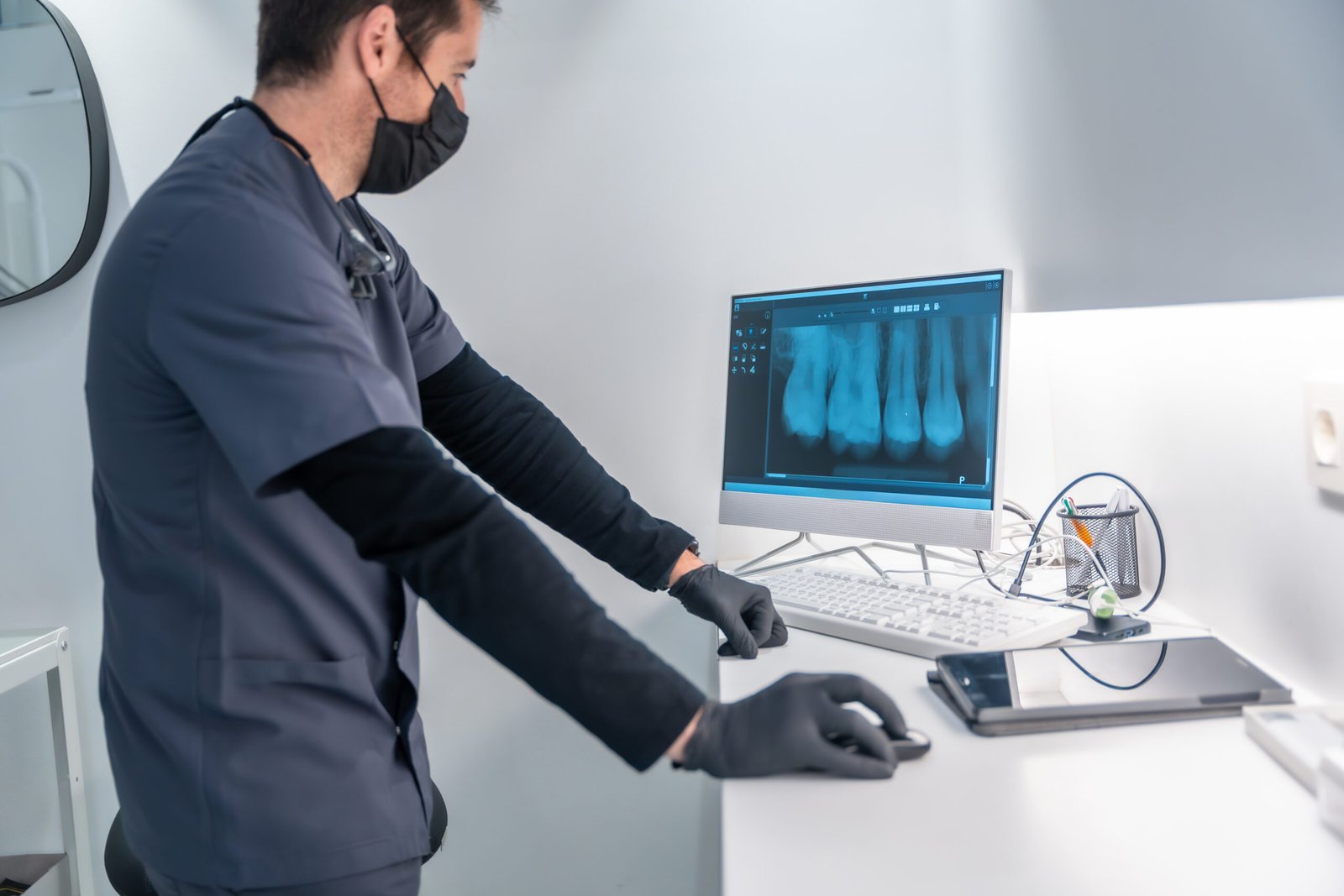 Dentist wearing mask and gloves analyzing a teeth x ray on a computer in a modern dental clinic