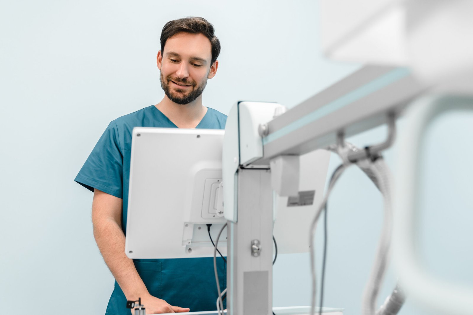 Doctor working looking at X-ray machine computer screen in modern clinic. Male radiologist sets up the machine to x-ray over patient. Medical equipment operator close-up in clinic