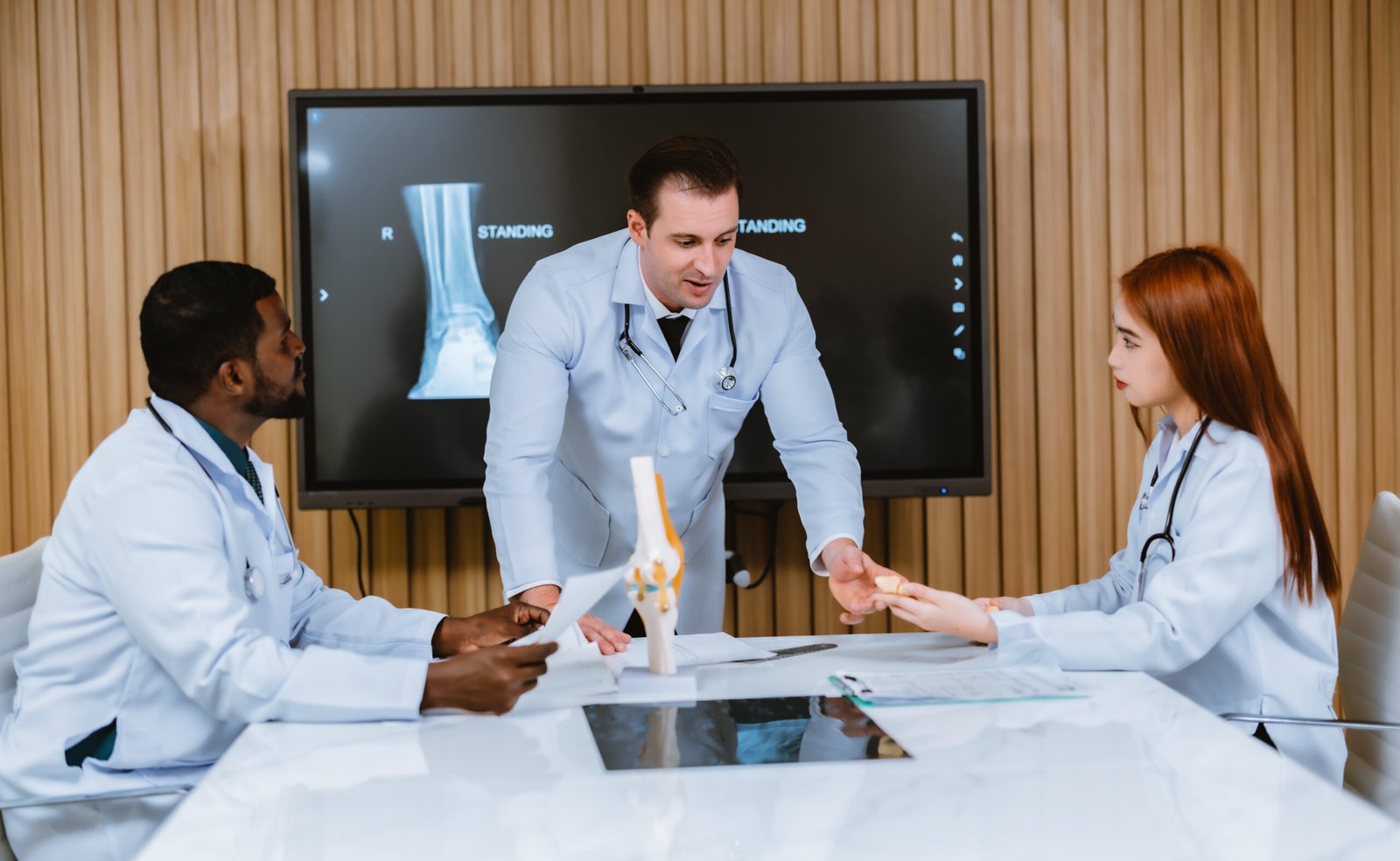 A multicultural boardroom discussion between the surgeon, radiologist on patient's case of ankle injuries. They examine, analyze MRI scans for the most effective, precise treatment plan and procedure