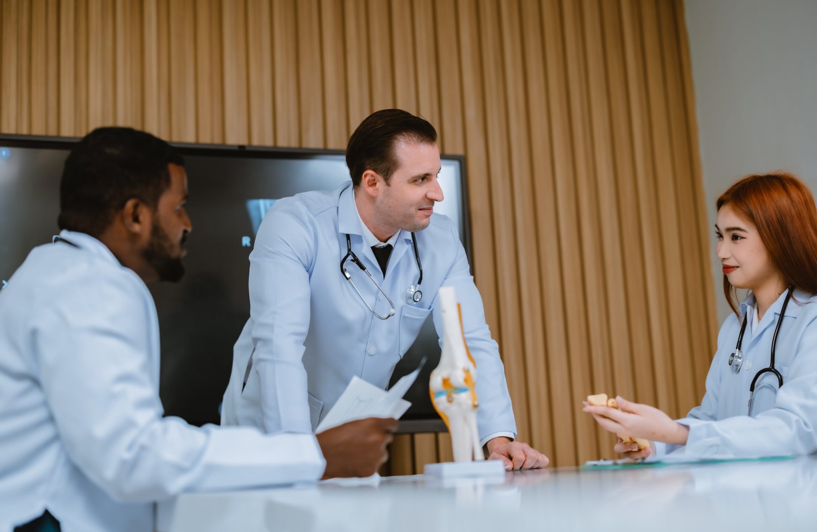 A multicultural boardroom discussion between the surgeon, radiologist on patient's case of ankle injuries. They examine, analyze MRI scans for the most effective, precise treatment plan and procedure