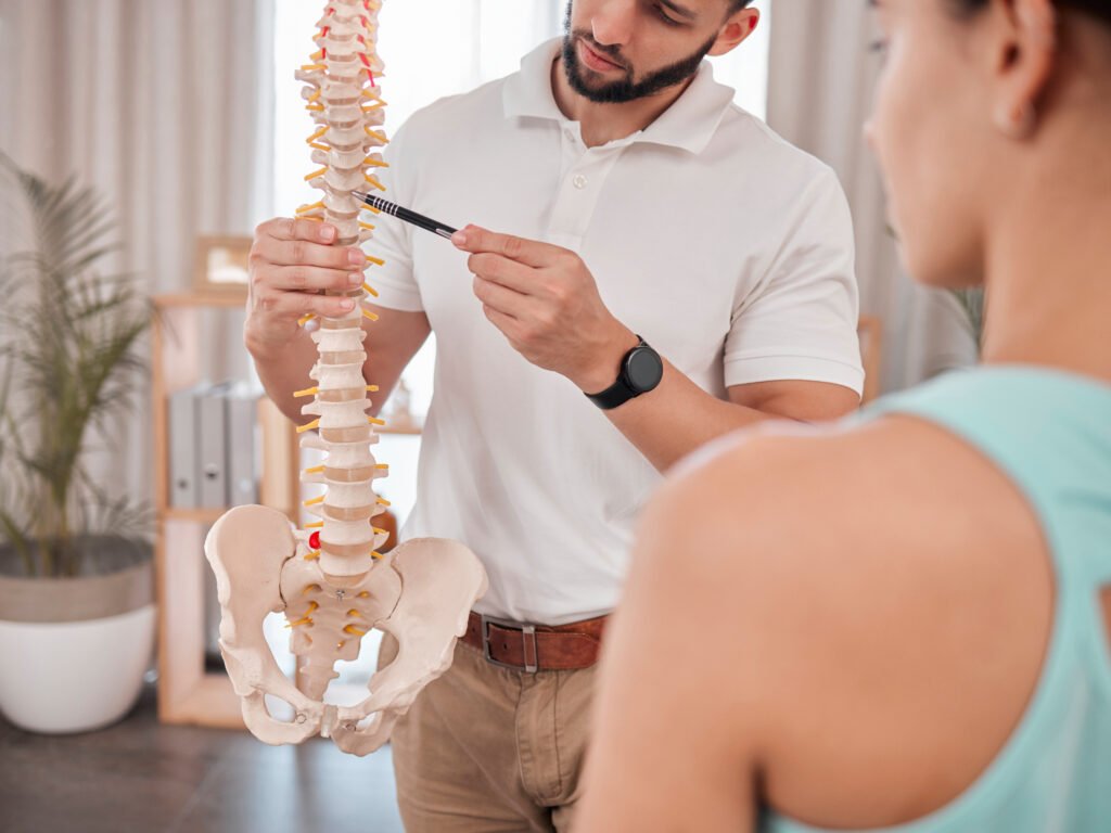 A specialist explaining spine alignment using a detailed spinal model to a patient, illustrating healthy vertebral posture and anatomy.