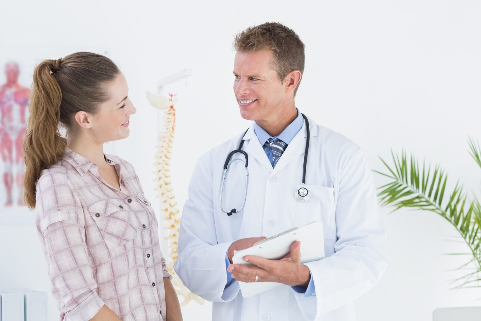 Happy doctor with clipboard talking to patient in clinic