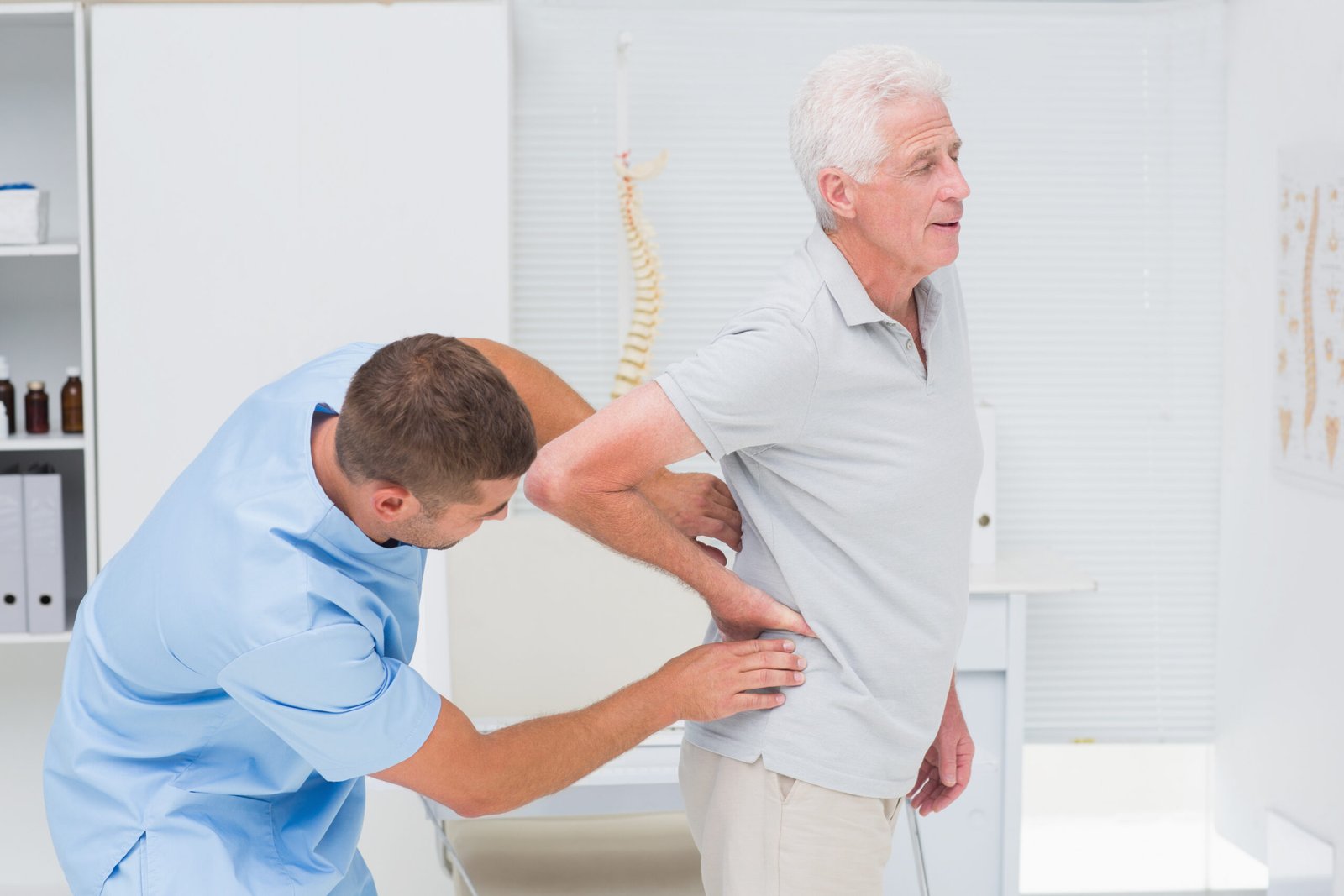 Physiotherapist giving back massage to senior man in clinic